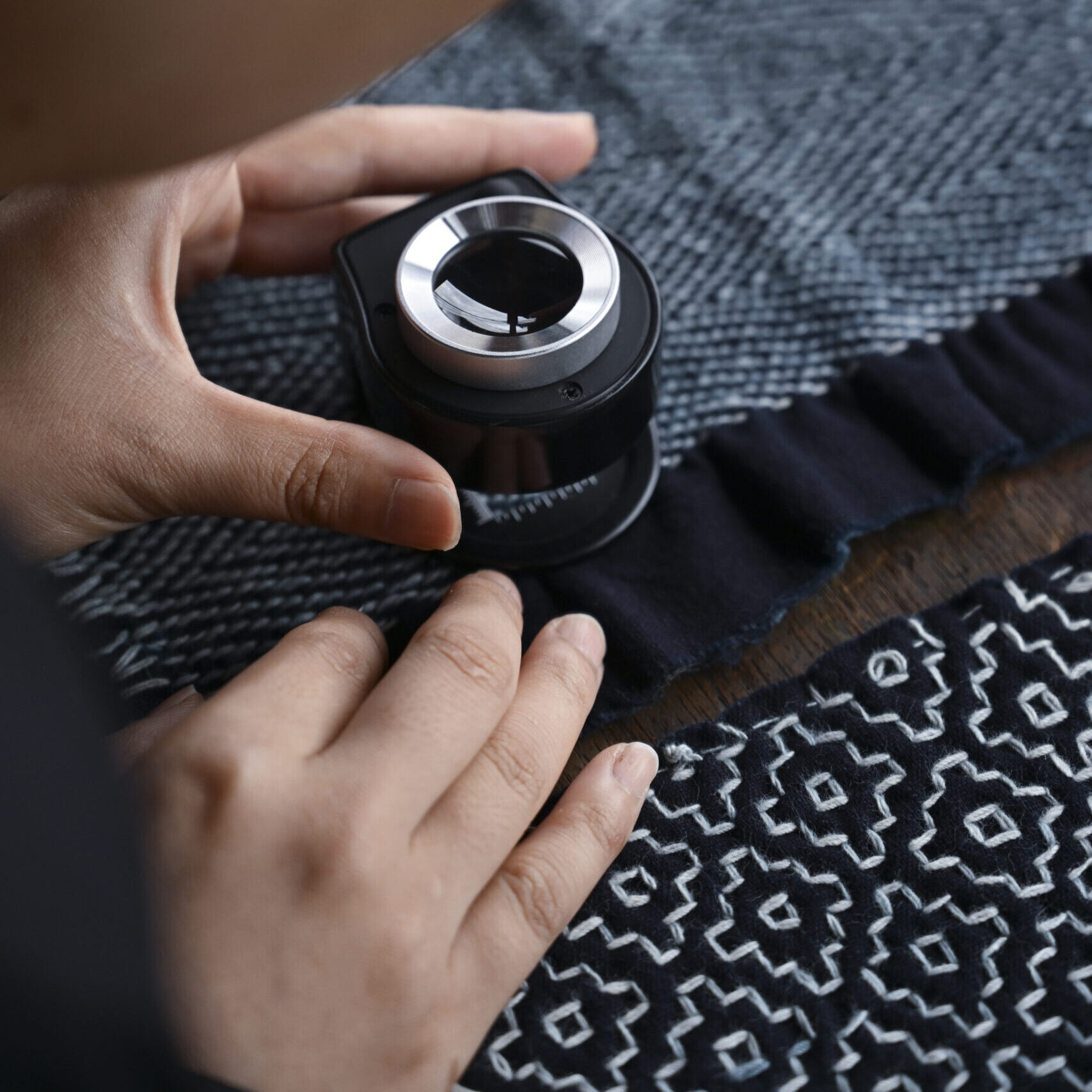 Hand holding a loupe over vintage boro textile with white sashiko stitching