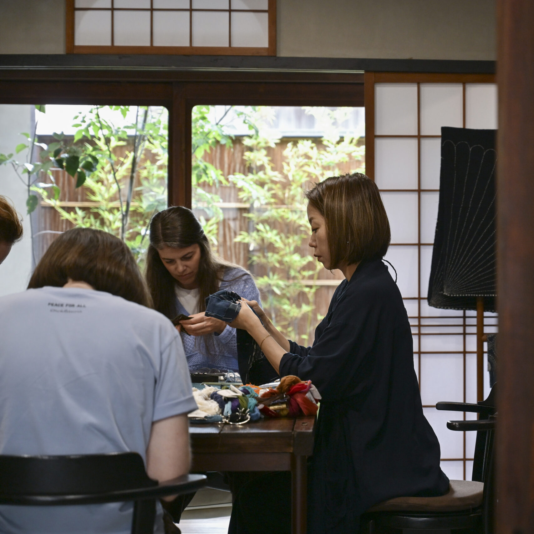 Participants and instructor stitching at a long table in the atelier, with a garden visible through the sliding windows