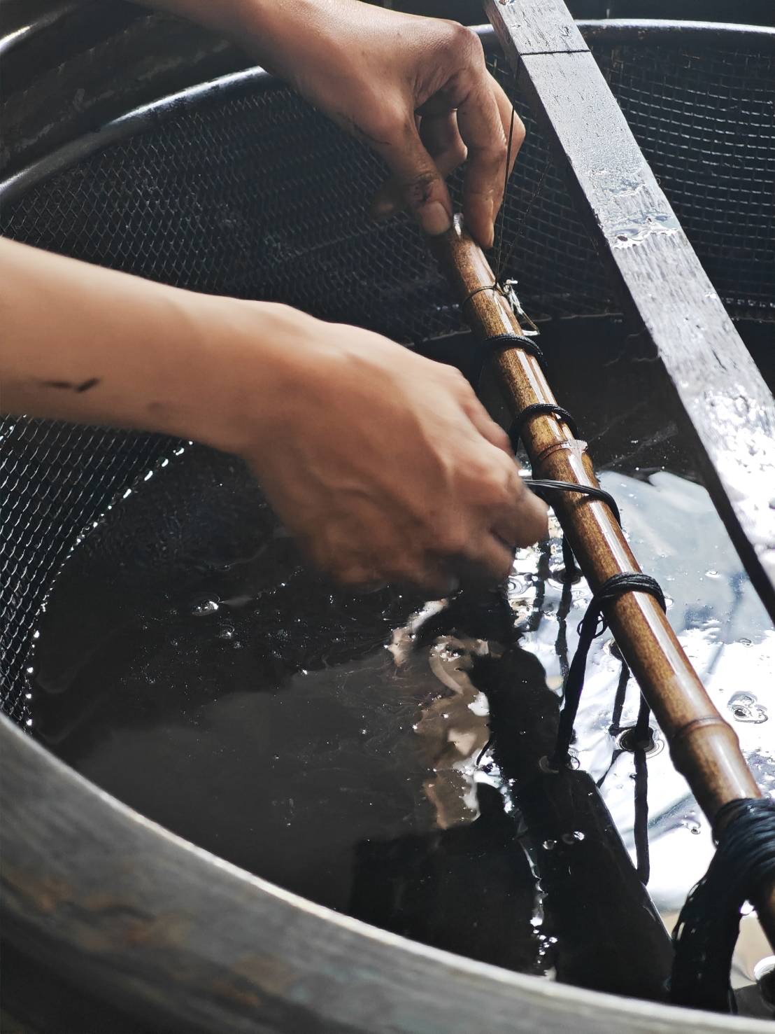 Hands dipping threads into an indigo dye vat